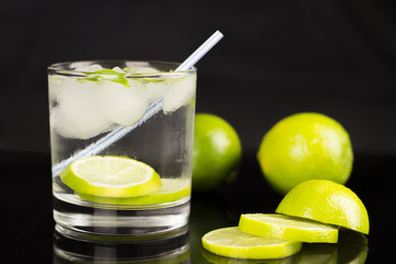 Alcohol drink (Gin Tonic cocktail) with lime and ice on black background with reflections