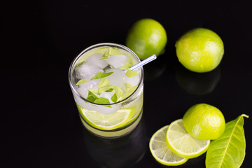 Alcohol drink (Gin Tonic cocktail) with lime and ice on black background with reflections