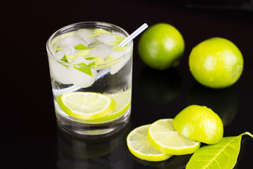 Fototapeta premium Alcohol drink (Gin Tonic cocktail) with lime and ice on black background with reflections