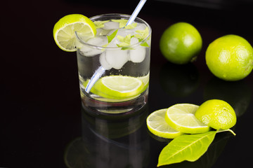 Alcohol drink (Gin Tonic cocktail) with lime and ice on black background with reflections