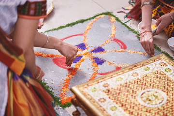 Women help coloring the traditional rice art (Rangoli) on the floor for indian wedding