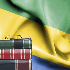 Education concept - Stack of books and reading glasses against National flag of Gabon
