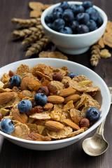 cereal flakes with blueberries and nuts on a dark wooden table, closeup