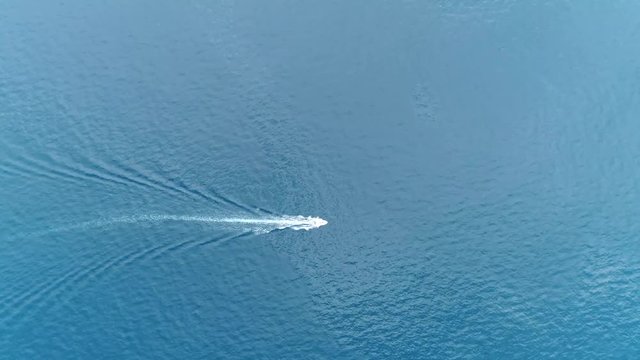 Aerial top down footage of speedboat powerboat moving fast over tropical azure blue colored ocean also showing the white foam left behind by the full powered propellers behind the boat 4k quality