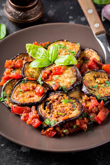 Fried eggplant slices with tomatoes, herbs and garlic, tasty vegetarian summer lunch. Grilled aubergine