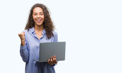 Young hispanic woman holding computer laptop screaming proud and celebrating victory and success...