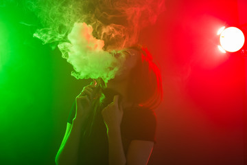 Young woman in black t-shirt vaping in red and green neon light