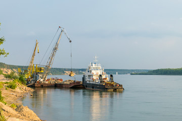 Fototapeta premium The crane unloads sand from the barge