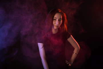 Young woman in neon light and smoke of e-cigarettes or vape on black background