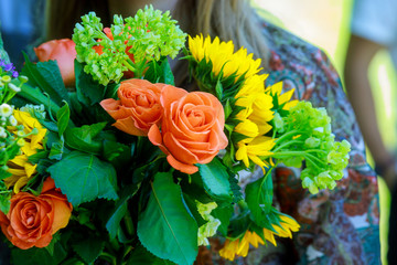 Young woman holding modern asymmetrical bouquet of flowers on the street near flower shop