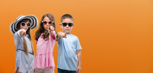 Group of boy and girls kids over orange background pointing with finger to the camera and to you,...