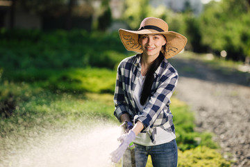 Beautiful young gardener woman watering garden in hot summer day