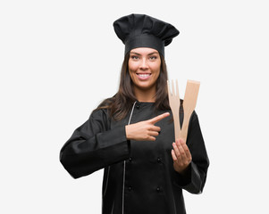 Young hispanic cook woman wearing chef uniform very happy pointing with hand and finger