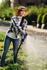 Beautiful young gardener woman watering garden in hot summer day