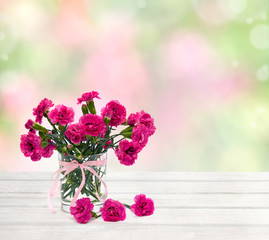 Bouquet of flowers pink carnations ( Dianthus caryophyllus ) in small vase on white wooden table on a blur natural background with space for text