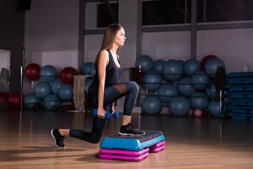 Fototapeta na wymiar Young woman performs step cardio with dumbbells in a gym