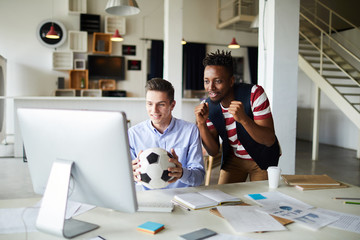 Two tense guys standing in front of computer monitor in studio and watching webcast of world...