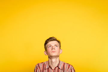 serious concentrated handsome man looking up. portrait of a young guy on yellow background popping...