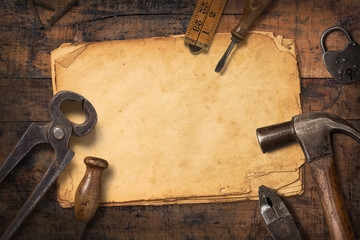 rustic crafting background with vintage tools and a stack of old stained paper on a wooden desk, flat lay / top view