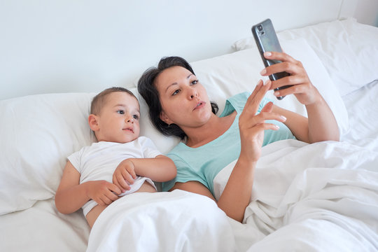 mom and baby lie together in bed and take selfies.