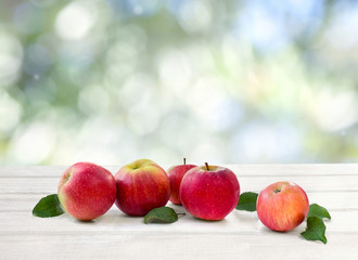 Ripe red juicy apples and leaves apple tree on white wooden table on a blur natural background with space for text