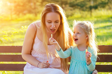 cute little blonde girl daughter eating french fries together with a beautiful mother in the park