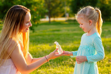 cute little blonde girl daughter in a blue dress with beautiful long-haired mother applying...