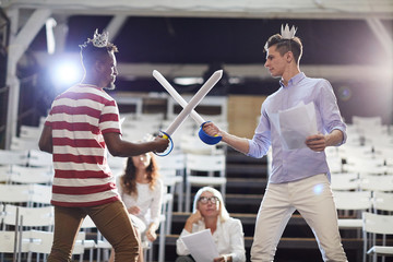 Two young princes in paper crowns fighting with paper swords during performance repetition on stage