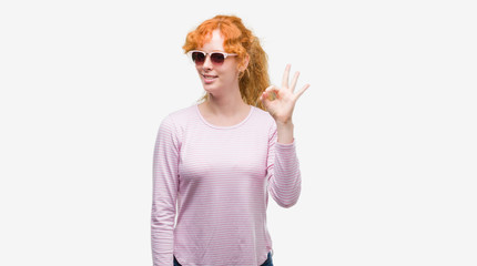 Young redhead woman wearing sunglasses doing ok sign with fingers, excellent symbol