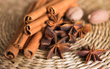 Closeup spices for mulled wine are on a straw stand. In the foreground are sticks of cinnamon and star anise, in the background is nutmeg