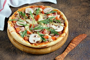 Homemade pizza with smoked meat, tomatoes, mozzarella cheese, portobello mushrooms, dried olives and arugula. Top view. 