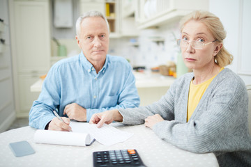 Aged modern couple sitting by table at home and counting family budget for the last month