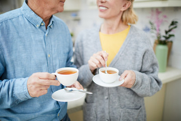 Senior spouses with cups of tea having talk in their kitchen by breakfast