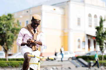 Handsome young Afro American man in casual clothes and sun glasses riding his bike and looking on the watch at time if he is not late