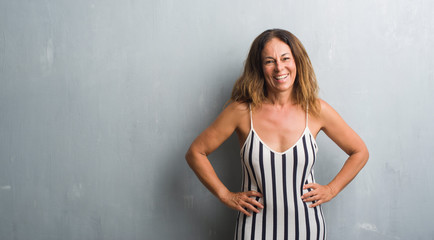 Middle age hispanic woman standing over grey grunge wall with a happy face standing and smiling...