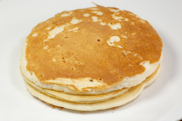 A stack of golden pancakes on a white plate sitting on a kitchen table waiting to be eaten