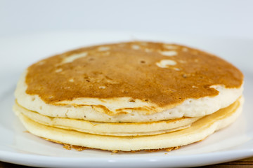 A stack of golden pancakes on a white plate sitting on a kitchen table waiting to be eaten