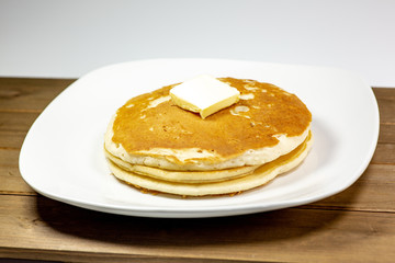 A square of butter laying onto of a stack of golden pancakes on the kitchen table waiting to be eaten
