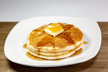Pancake with a square of butter and syrup on a kitchen table waiting to be eaten