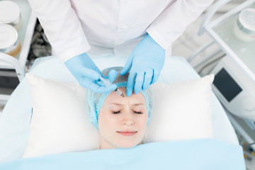 Obraz na płótnie Canvas Cosmetician making revitalizing injection in forehead of her client during beauty procedure