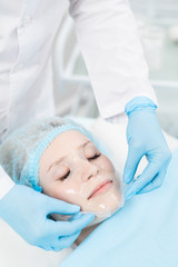 Fototapeta premium Cosmetician in gloves taking transparent fabric purifying mask off relaxed client face