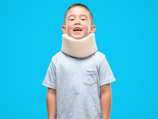 Dark haired little child injured wearing neck collar with a happy face standing and smiling with a confident smile showing teeth