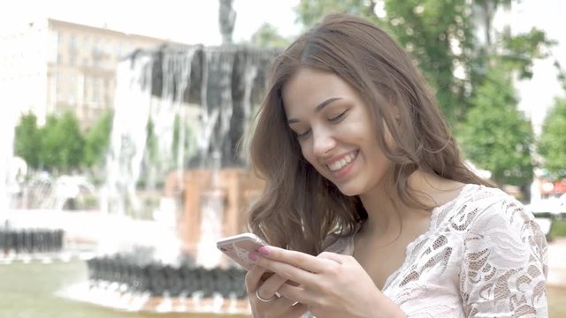 Attractive young woman using her touch screen mobile cell phone and smiling to herself