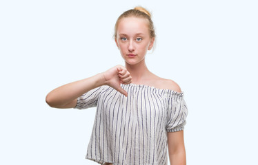 Blonde teenager woman wearing a bun with angry face, negative sign showing dislike with thumbs down, rejection concept