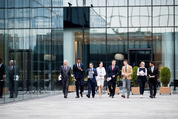 Large group of business people walking along modern business center and talking in urban environment - obrazy, fototapety, plakaty