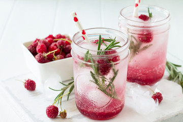 SOFT DRINKS. Refreshing summer drink raspberry with rosemary and ice. Glasses with cold and healthy beverage on a wooden kitchen table.