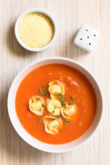 Homemade fresh cream of tomato soup with tortellini garnished with fresh oregano leaves, photographed overhead with natural light (Selective Focus, Focus on the top of the soup)