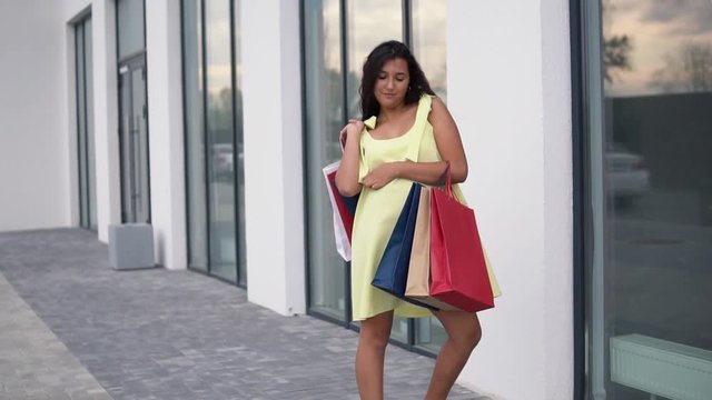 Beautiful girl model in a long dress after shopping with colored bags in hands having a good mood. slow motion.
