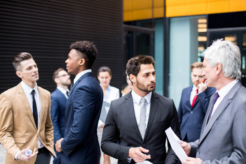 Young and senior financiers in suits having talk about market development among their colleagues