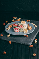 Traditional oriental sweets and nuts: hazelnuts, cashews on a dark wooden background. Turkish dessert is the Rakhat locus. View from above. Place under the text.
